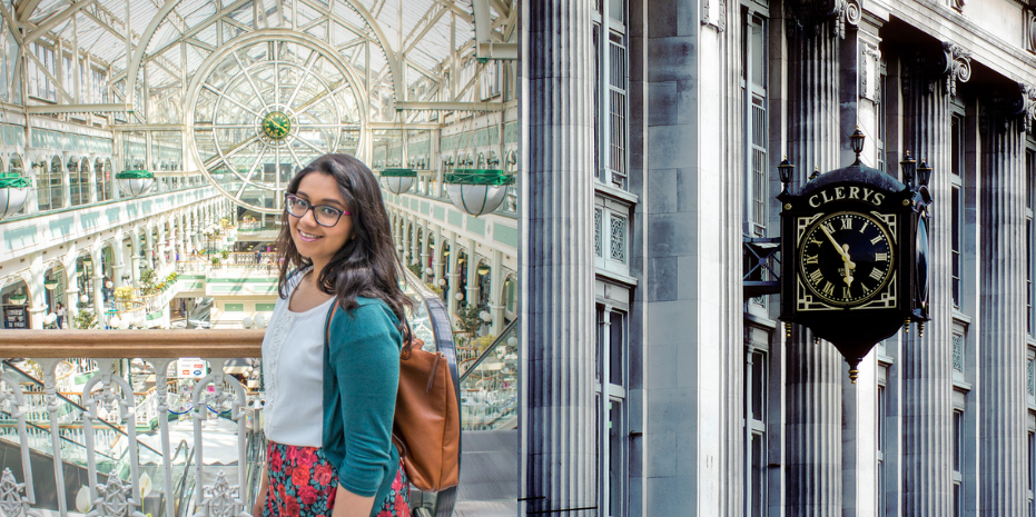 Woman Stands smiling in front of St Stephens Green Shopping Centre Clock in Dublin and Clerys Clock on O Connell Street